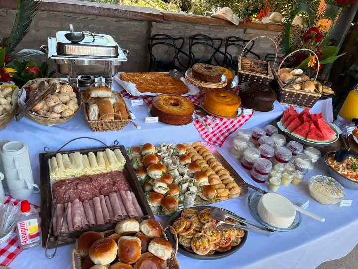 Mesa comprida com pães, frutas, bolos, bebidas e louças preparadas para o café da manhã