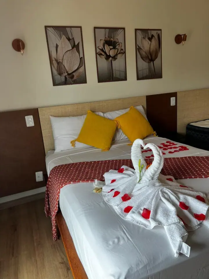 Quarto claro com cama de casal, detalhes amarelos e toalhas dobradas
