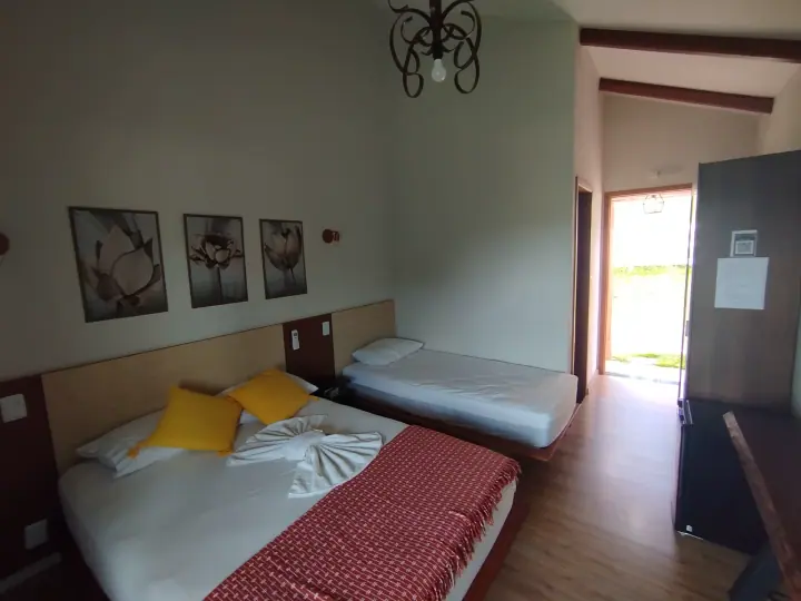 Acomodação clara com uma cama de casal, uma cama de solteiro, madeira e porta aberta para o jardim