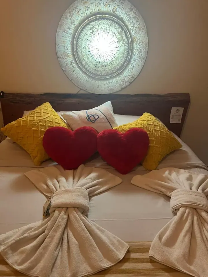 Cama de casal com cabeceira de madeira, almofadas amarelas e iluminação lateral